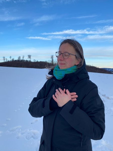 Ayurveda hat mir so geholfen. Ich stehe mit geschlossenen Augen und den Händen vor dem Herz verschränkt auf einer schneebedeckten Wiese.